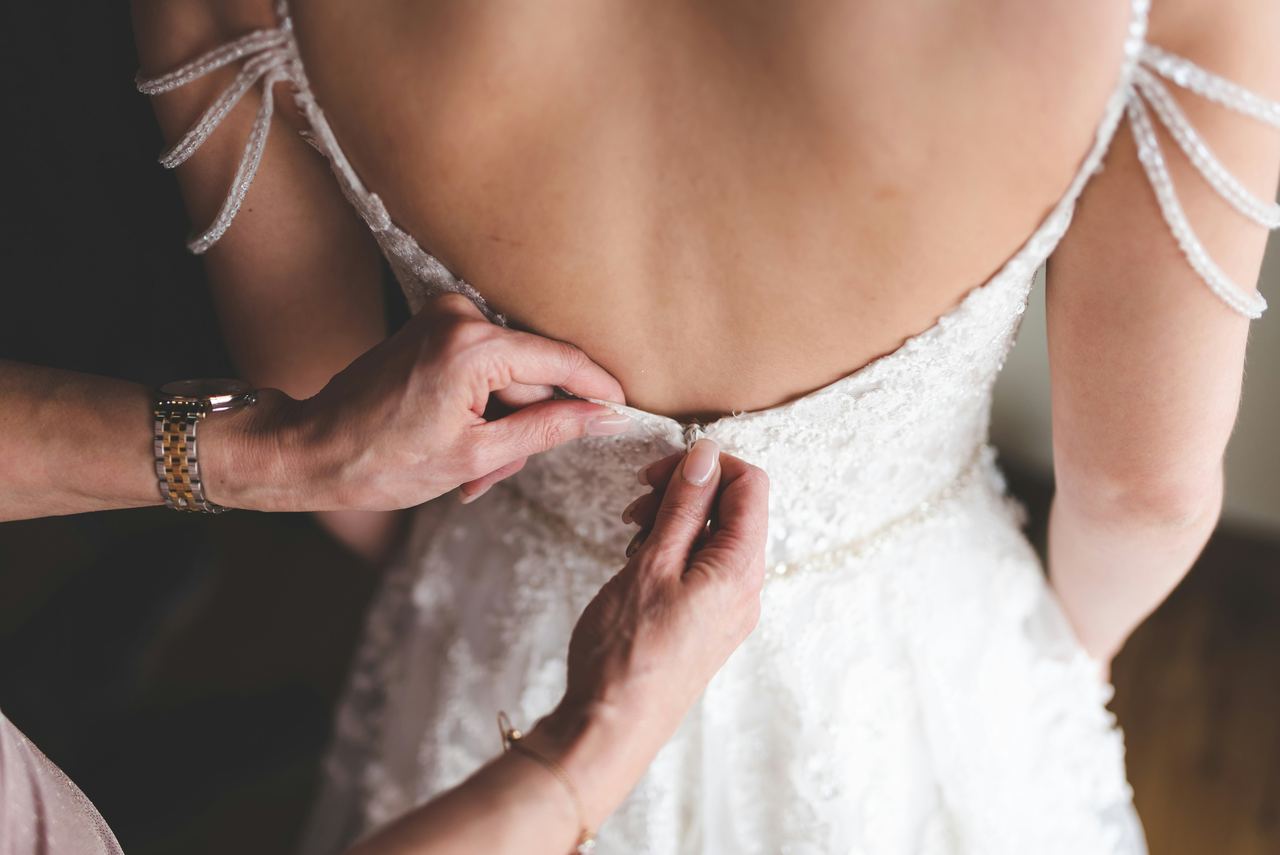 Zwei Hände schließen den Rücken eines Brautkleids aus Spitze